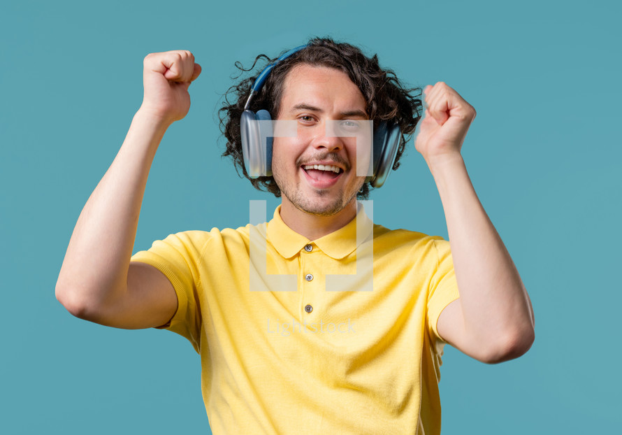 Positive handsome man listening music, enjoying dance with trendy modern headphones on blue studio background. Radio, wireless modern sound technology, online player. High quality