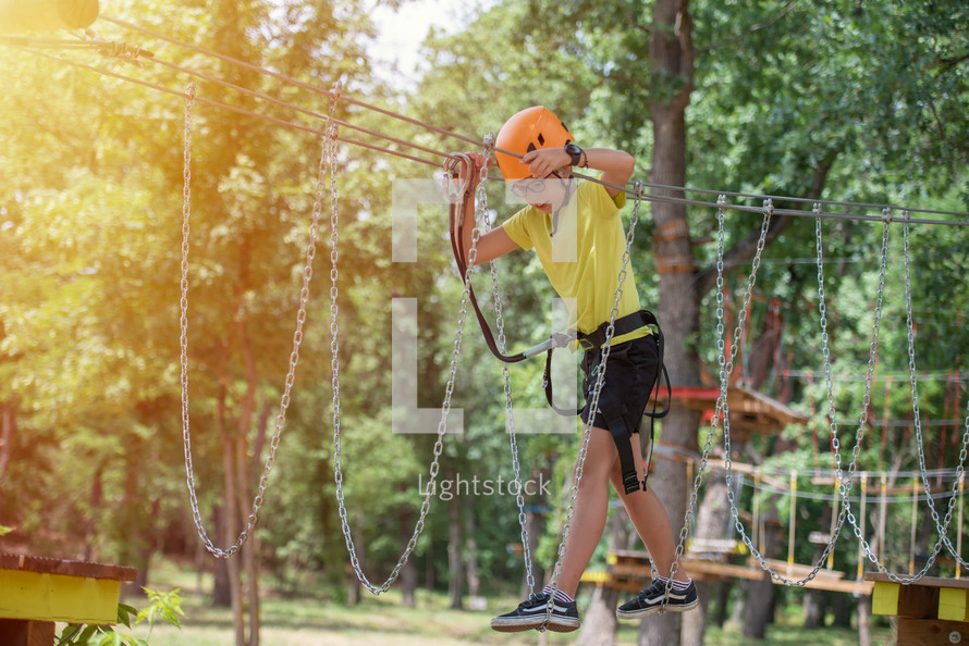 Boy enjoys climbing in the ropes course adventure. Happy boys playing at adventure park holding ropes and climbing wooden stairs