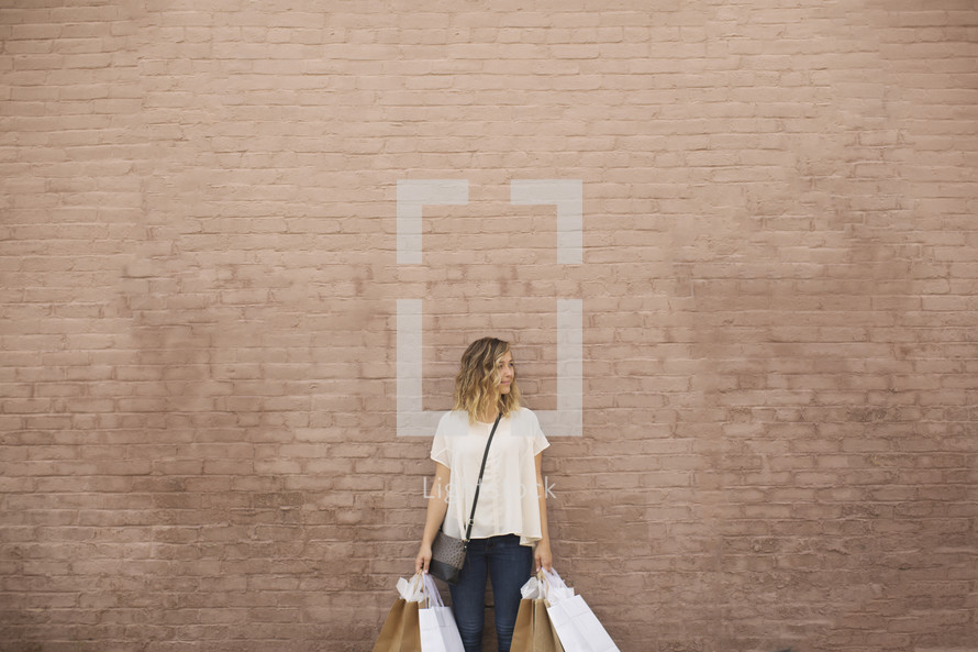 a woman holding shopping bags against a brick wall.