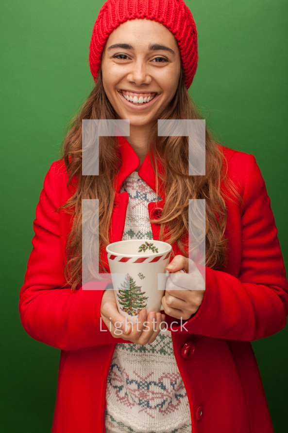 a woman in a red trench coat holding a Christmas mug 