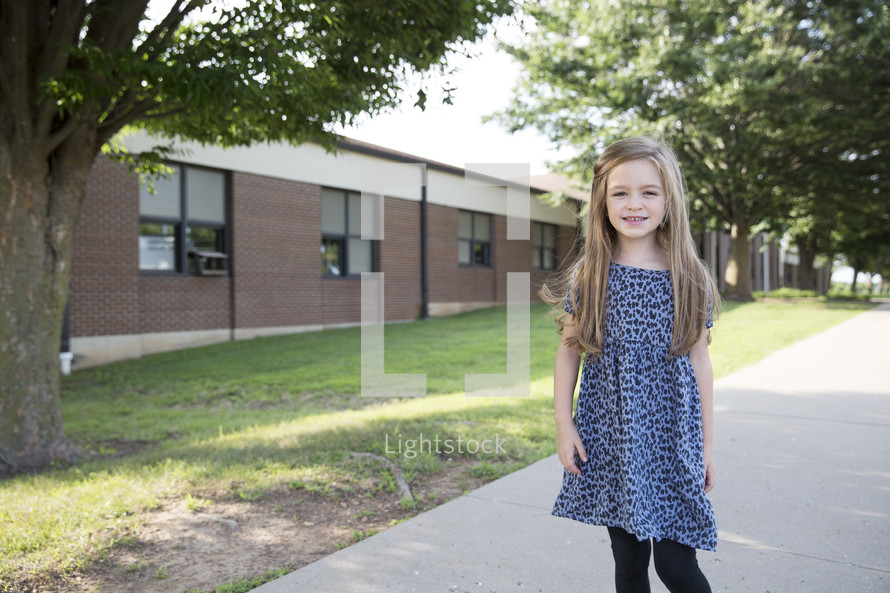 A little girl walking along a sidewalk next to a school.