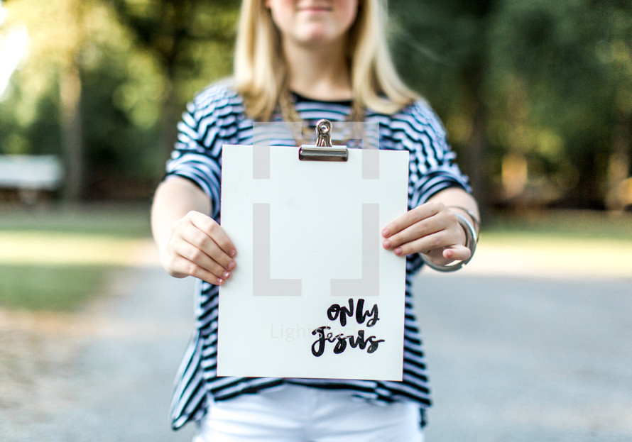 A young woman holding out a clipboard reading, "only Jesus."