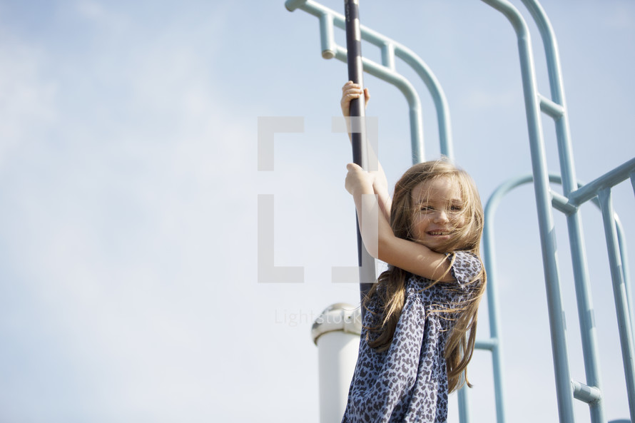 A little girl sliding down a pole on the playground.