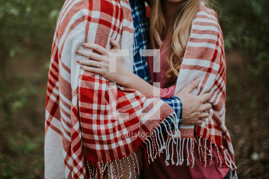 a couple snuggling wrapped up in a plaid blanket 