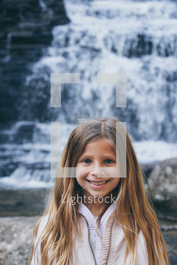 smiling girl standing in front of a waterfall 