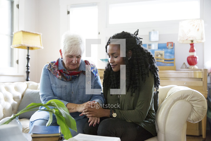 Mature woman and young woman praying together in a home. 
