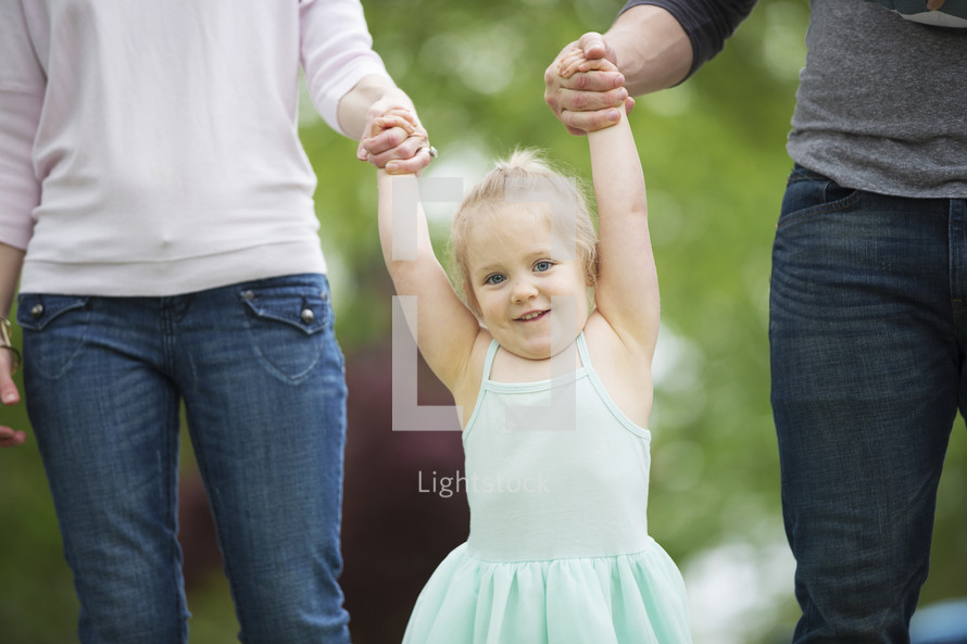 a toddler swinging holding mother and father's hands 