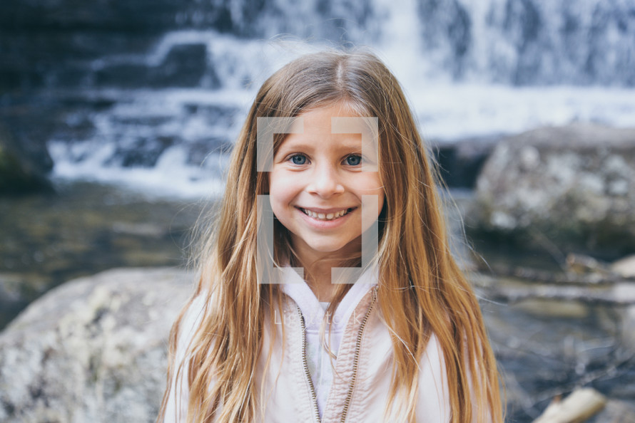 smiling child standing in front of a waterfall 
