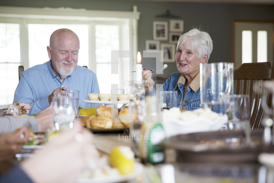 An older couple eating at the dinner table.