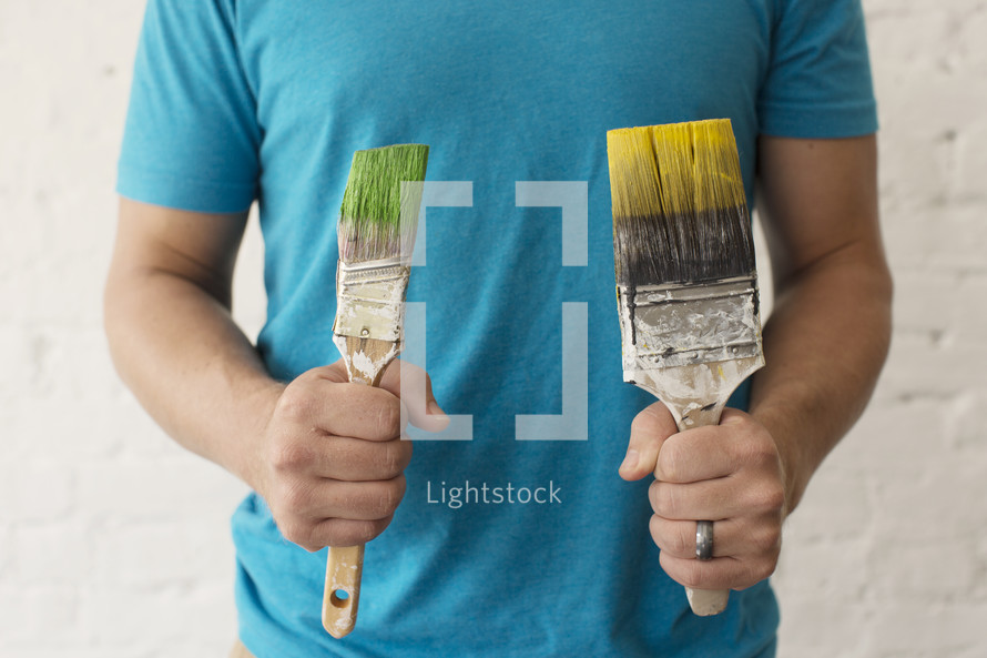 A man holding two paint filled paint brushes.