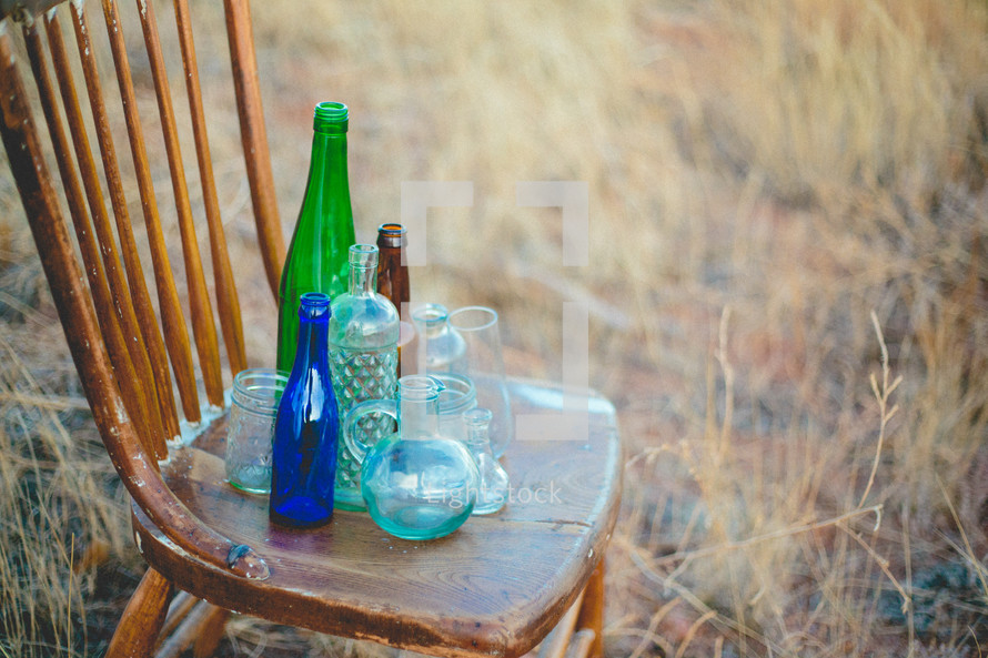 old glass bottles on a wood chair outdoors 