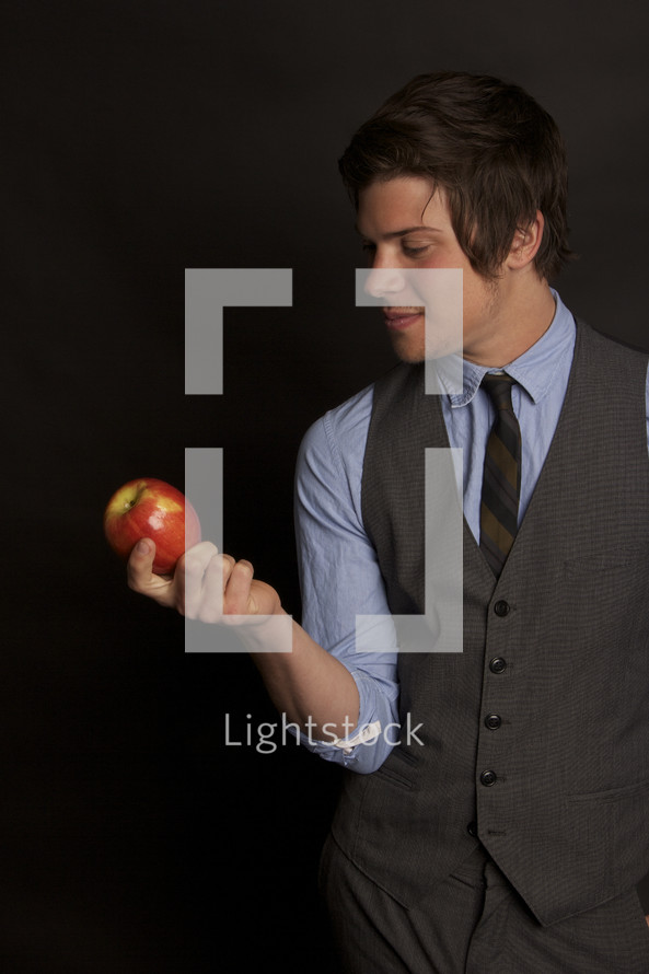 man in a vest and tie holding an apple 