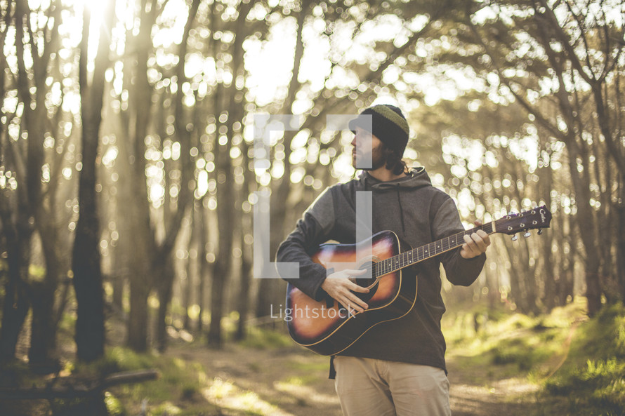 a man playing a guitar in a forest 