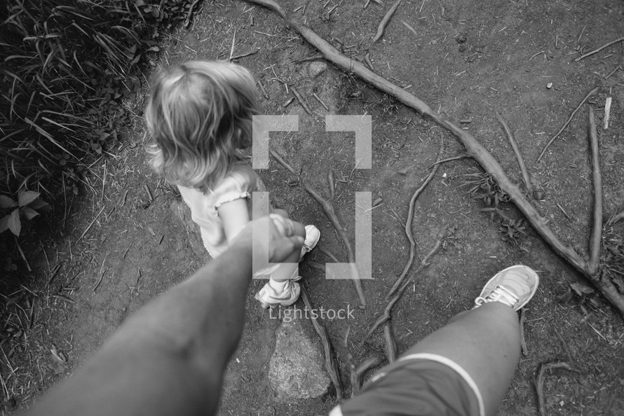 Parent holding a child's hand while hiking on a dirt  trail.