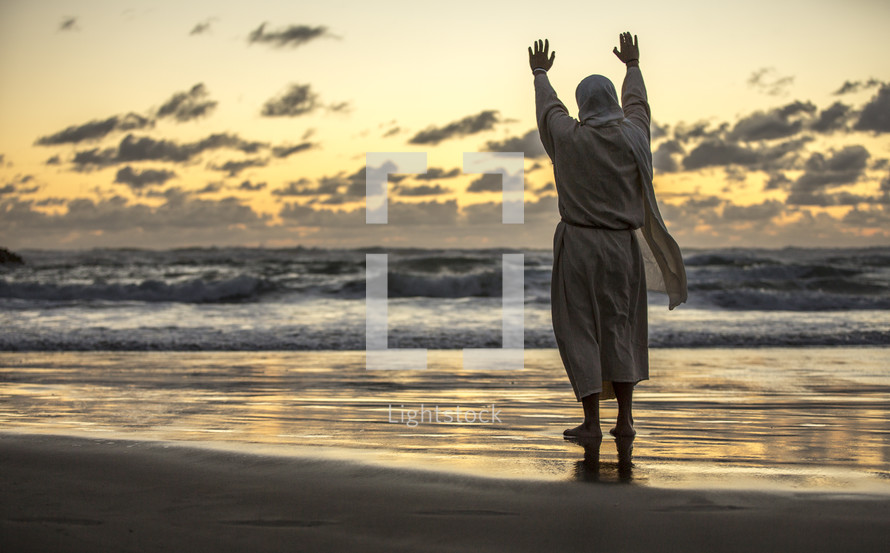 Jesus standing with raised hands on a shore at sunset 