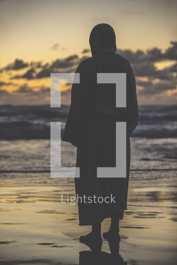 Jesus in a robe standing on a shore at sunset 