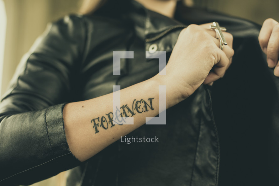 woman in a leather jacket with a tattoo of the word Forgiven 