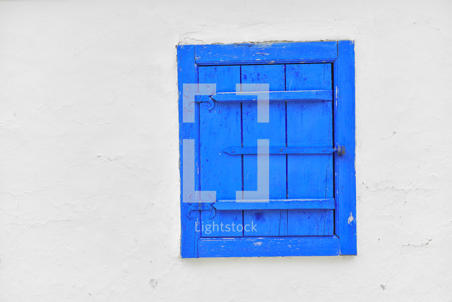 Closed vintage blue window on white wall of old house in Romania