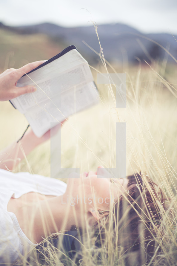 Woman laying in a field of grass reading the Bible.
