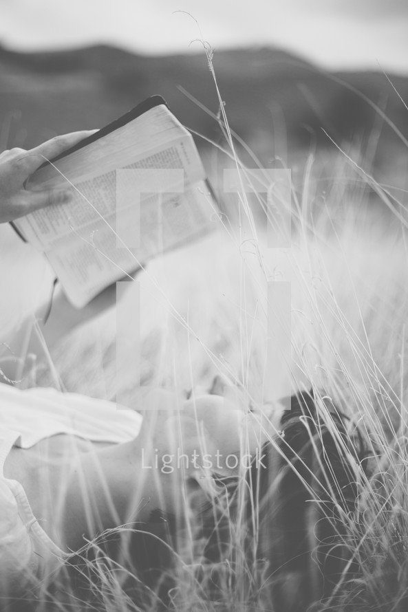 Woman laying outside in a field of grass reading the Bible.