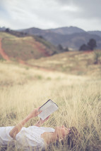 Woman laying in a field of grass, reading the Bible.