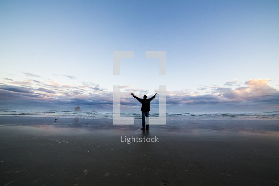 Man on a beach with arms raised toward sky.