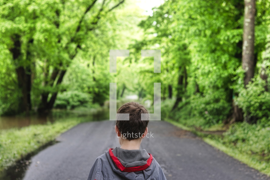 a boy standing alone on a rural road 