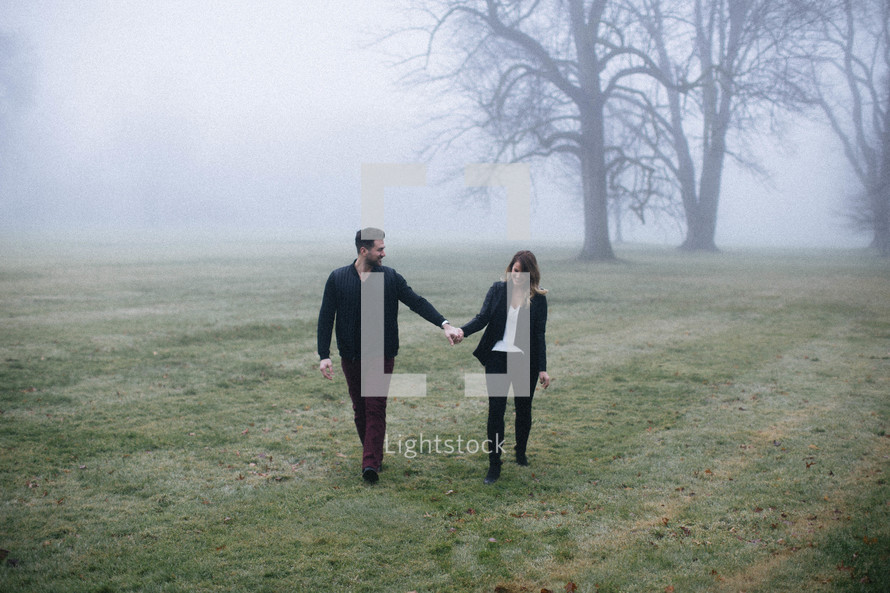 couple holding hands walking in a foggy field 