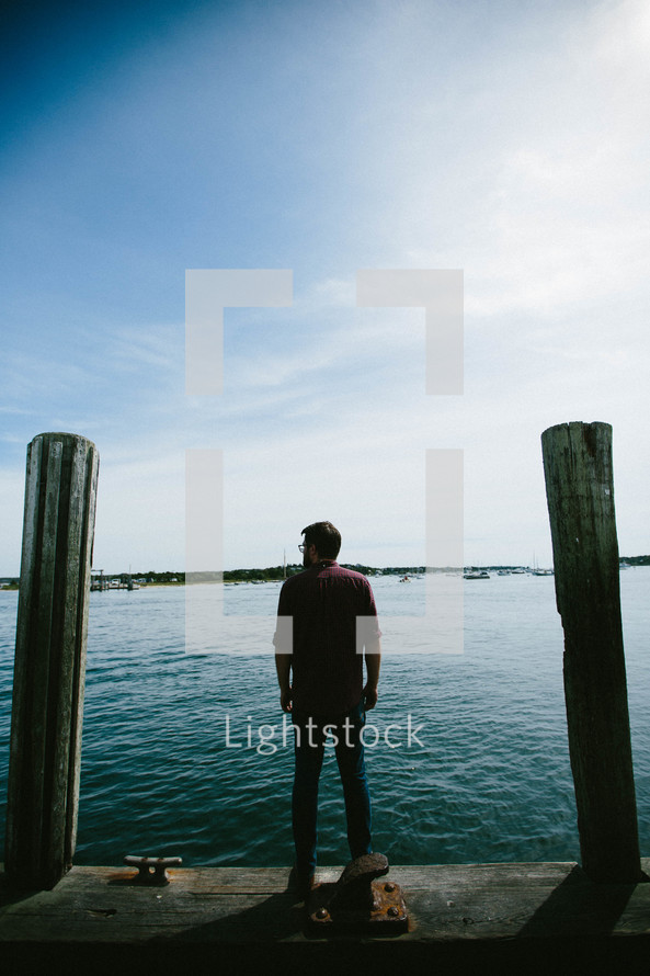 a man standing on a dock looking out at a harbor 