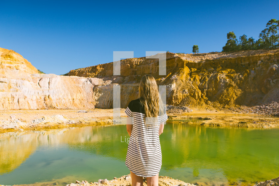 A girl standing near a pool of water in a quarry.