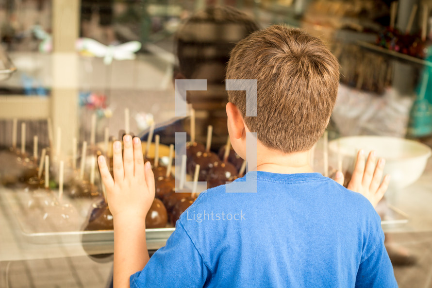 child looking through a window at candy apples 