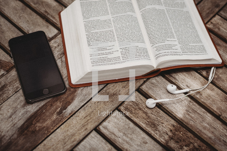 smartphone, earbuds, and an opened Bible 