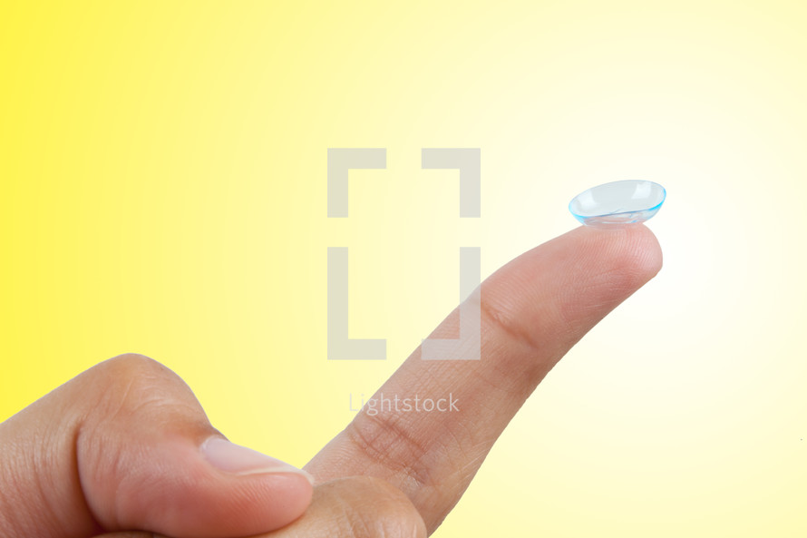 Contact lens on finger isolated on yellow background