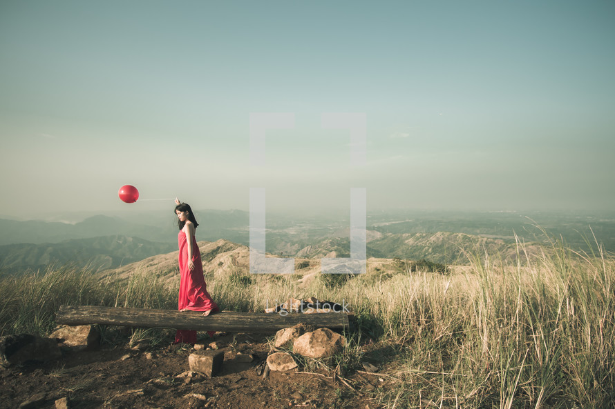 a woman on a mountaintop in a red dress holding a red balloon 