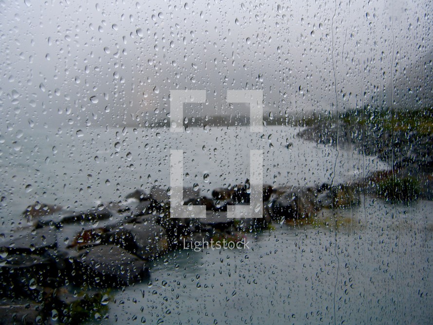 rain drops on a window with view of a shore 