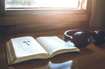open Bible with earphones for morning devotion on wooden table with sunlight