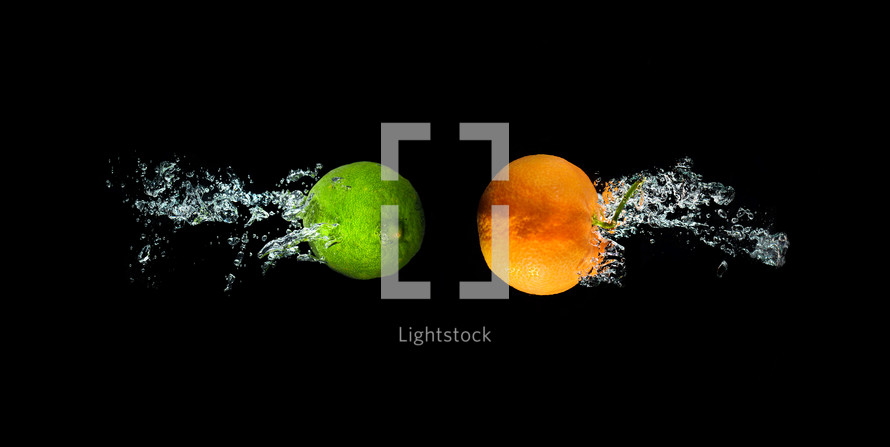 Fresh lime and orange in water with air bubbles water splash isolated on black