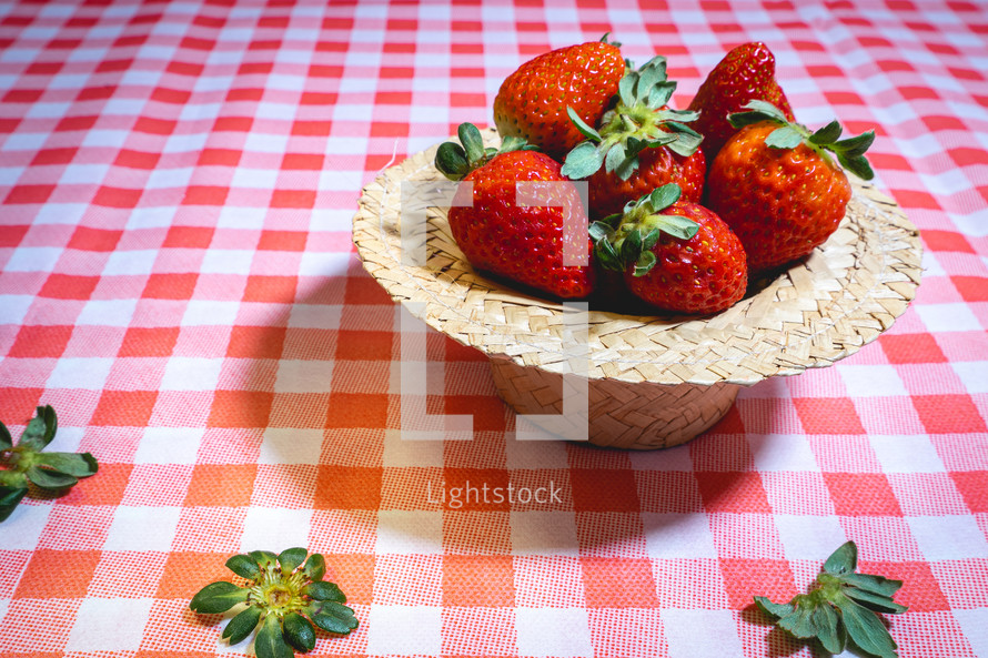 Fresh strawberries decorated on a straw hat. on a red picnic blanket.