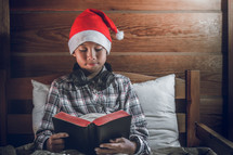 a boy in a Santa hat reading a Bible 