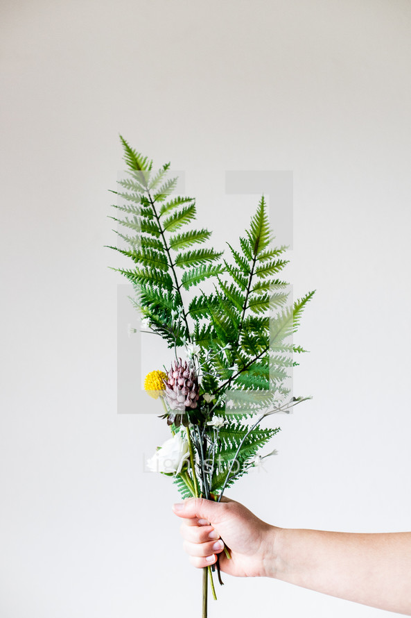 hand holding out a bouquet of flowers and ferns 