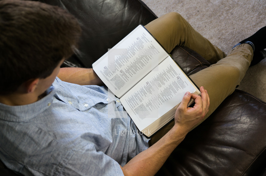 a man sitting on a couch reading a Bible 