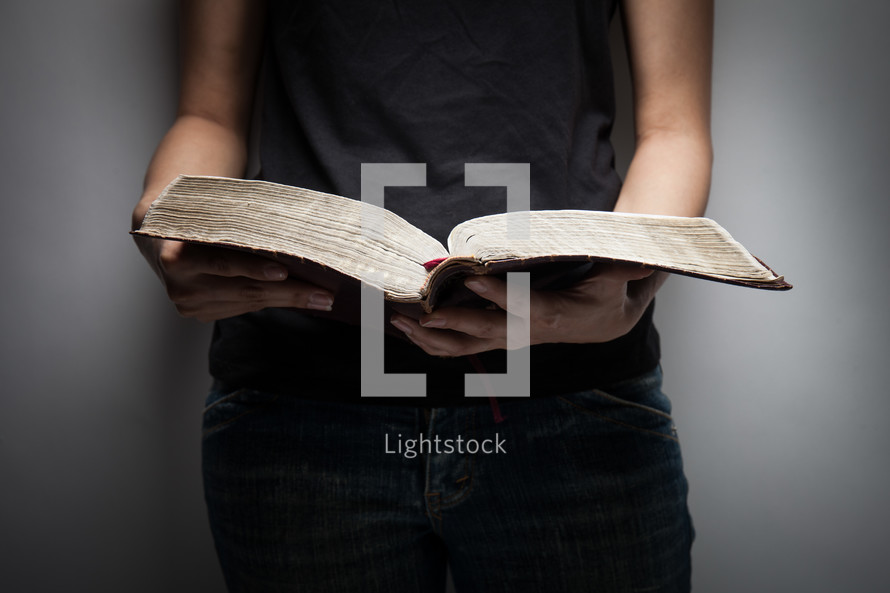 torso of a young woman in jeans and a tank top reading a Bible 