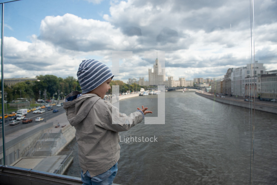toddler boy standing in front of a river on a bridge 