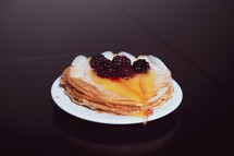 Stack of thin pancakes poured with honey and decorated with fresh blueberries side view with selective focus and dark background with copy space