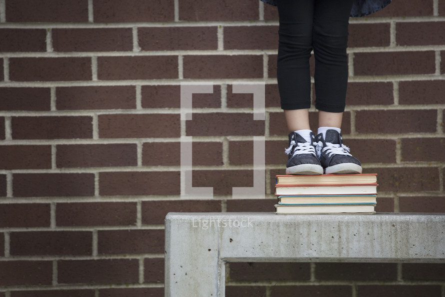 a child on a bench standing on a stack of books while waiting for school to start 