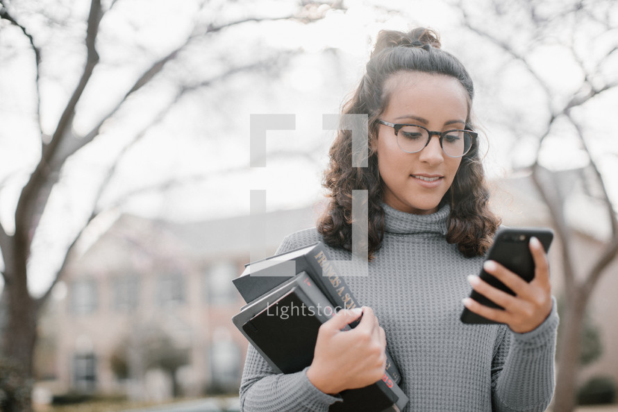a young woman holding a stack of books and holding a cellphone 