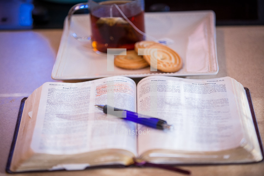 pen on an open Bible and tea with cookies 