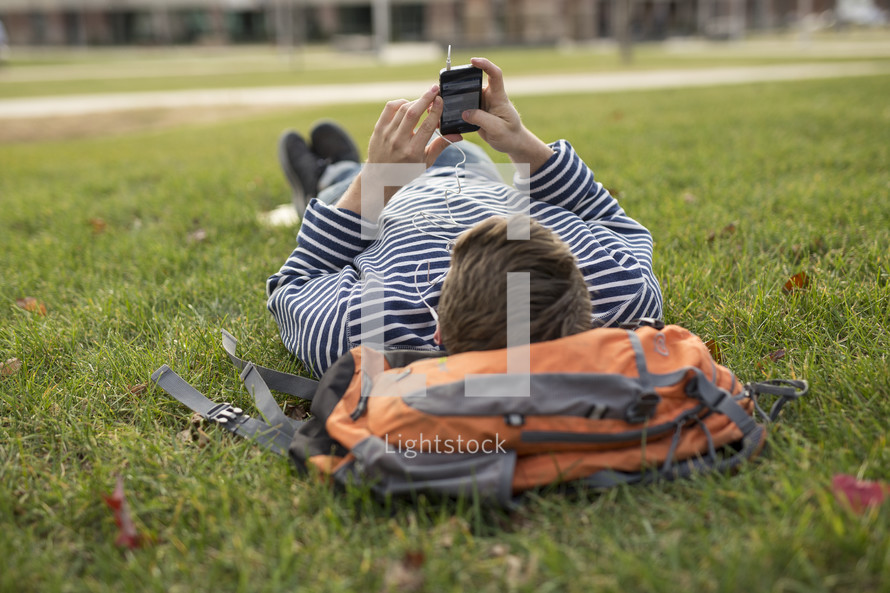 a college student lying in the grass listening to a podcast 