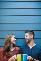 A young man and woman drinking coffee together near a blue wall.