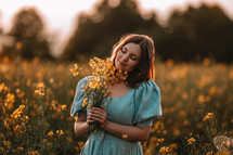Portrait of attractive woman posing in blooming canola flowers field. Elegant girl in retro dress with bouquet, countryside nature place. Rapeseed meadow, vintage outfit, spring season